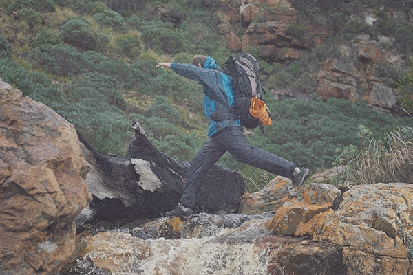 a man in hiking gear jumping over a stream